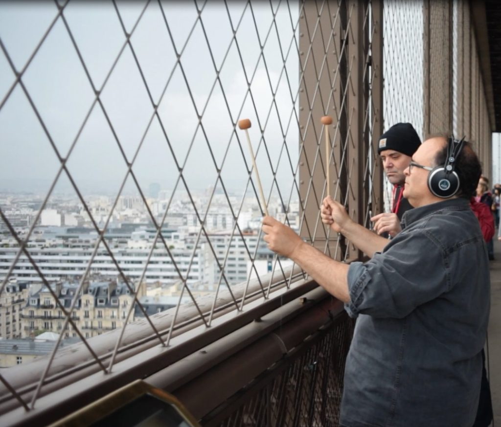 COMPOSER JOSEPH BERTOLOZZI AT FENCE WITH MALLETS AT THE EIFFEL TOWER, Image c. 2013, Blue Wings Press